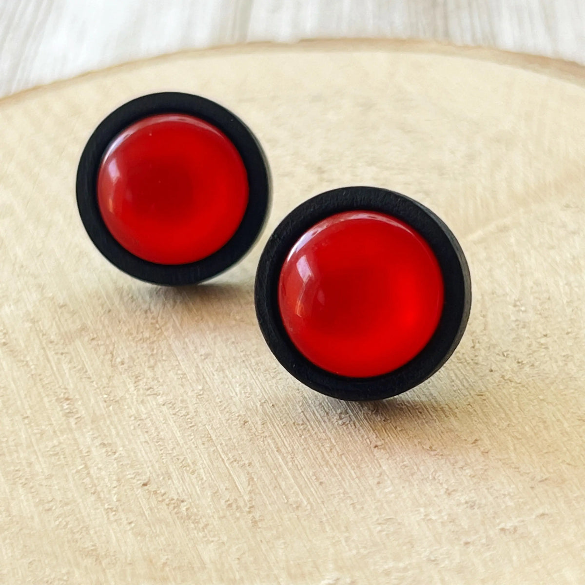 Pair of red circular earrings with black rims on a wooden surface