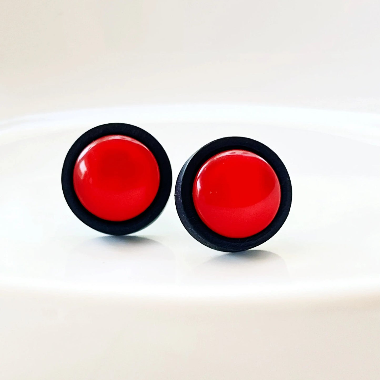 Round red resin stud earrings with black wood border displayed on a white dish