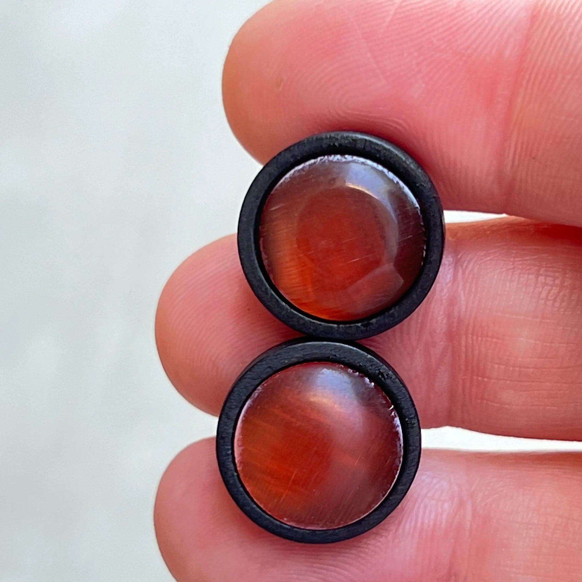 Pair of rust orange glass earrings with black wood held between fingers against a white background