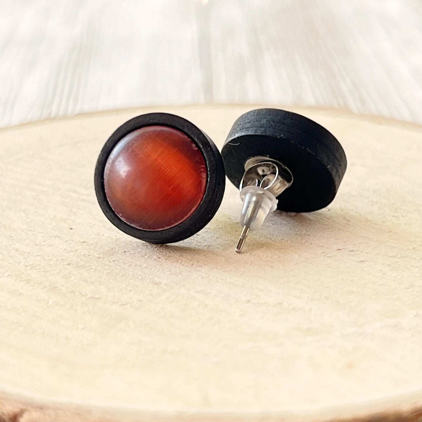 Round earrings with orange center and black outer rim on a wooden surface