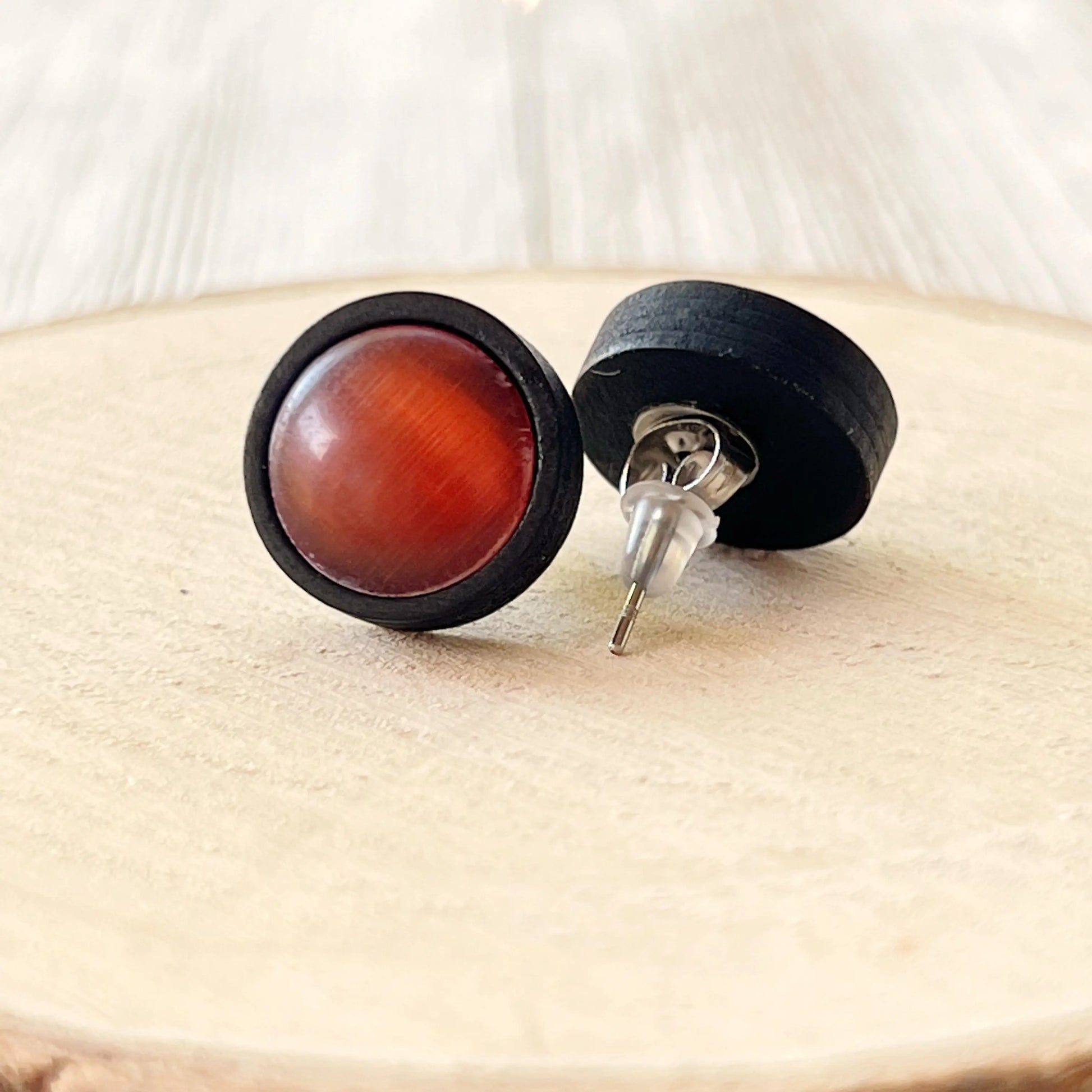 Round earrings with orange center and black outer rim on a wooden surface