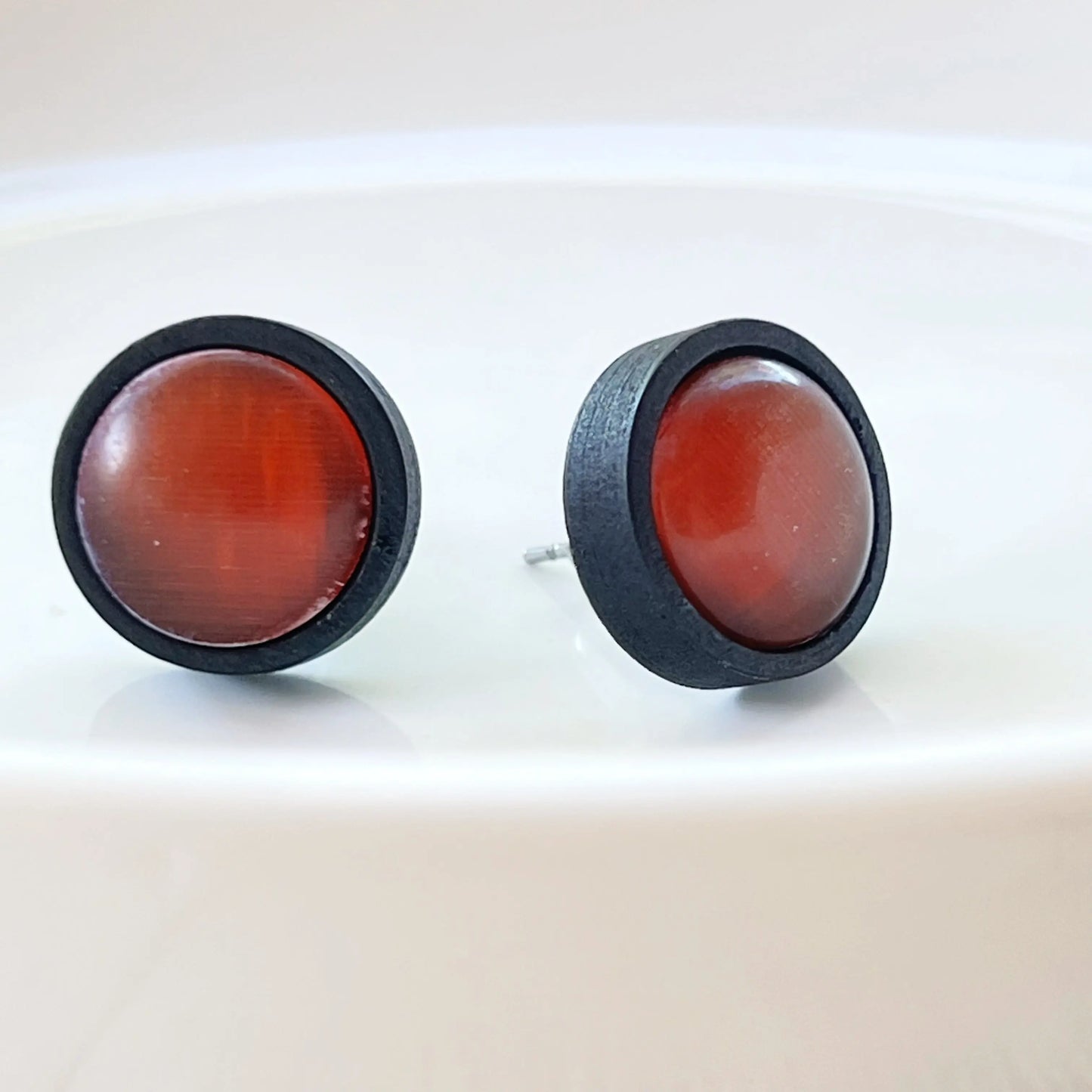 Round rust orange glass stud earrings with black wood border displayed on a white dish