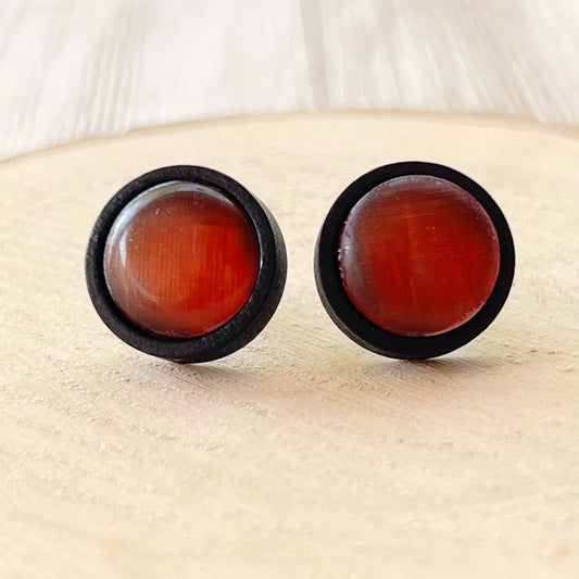 Pair of round earrings with orange glass on a beige surface