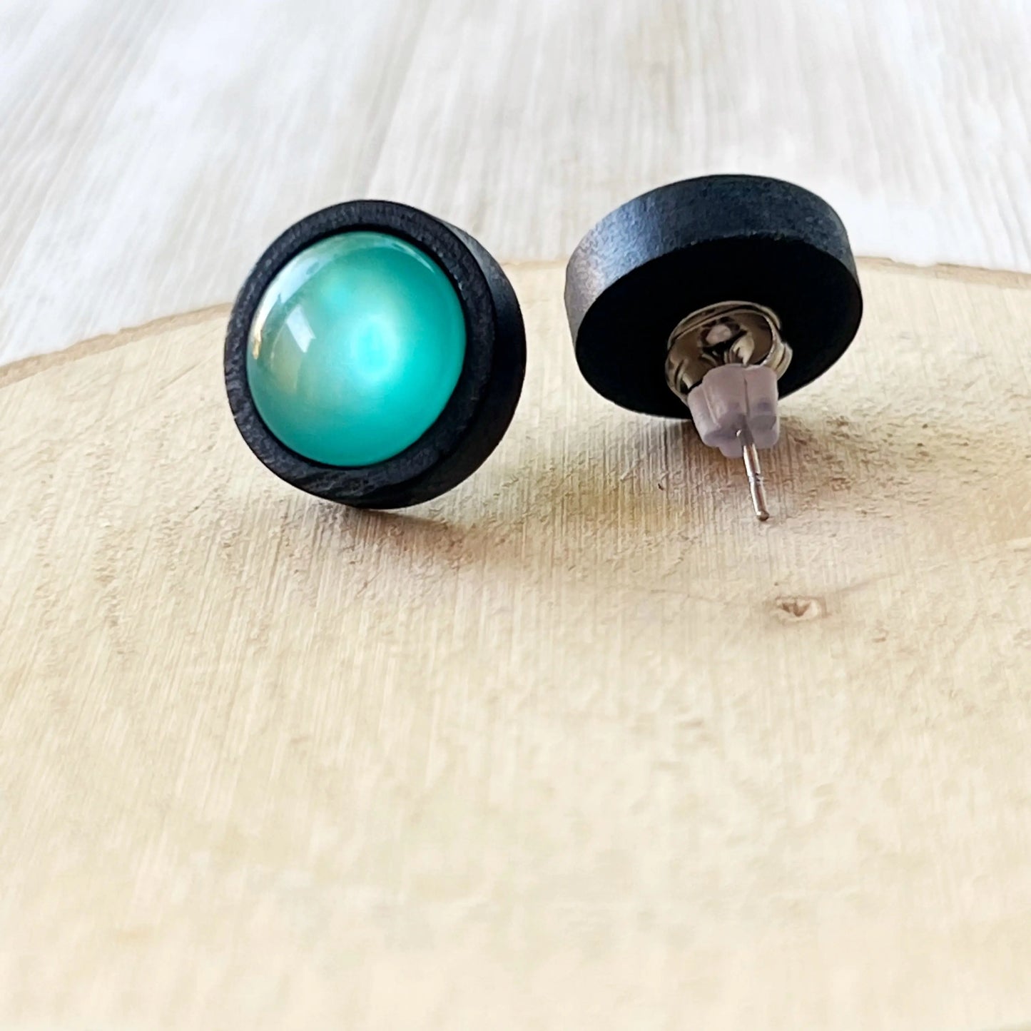 Round black wood stud earrings with glossy teal resin centers showing backside 