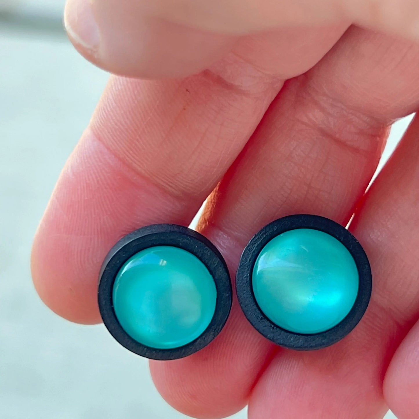 Round black wood stud earrings with glossy teal resin centers shown in hand