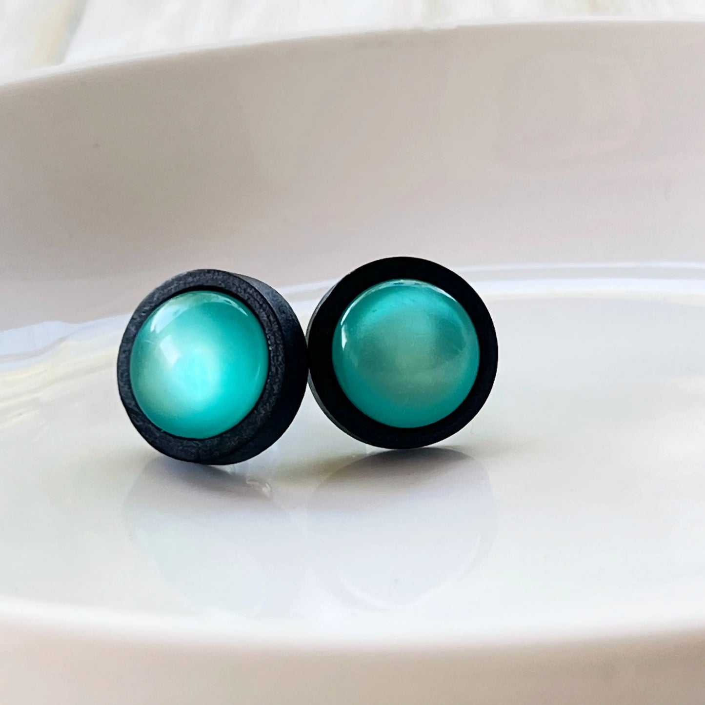 Round black wood stud earrings with glossy teal resin centers shown on white tray