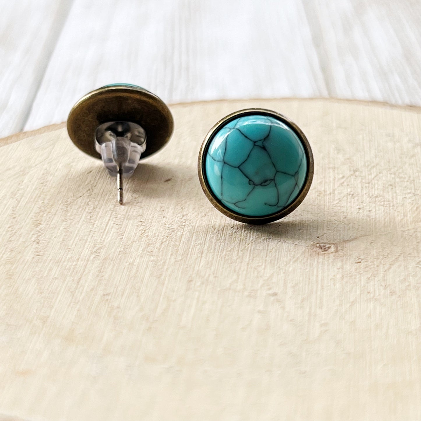Backside of round turquoise brass stud earrings displayed on a light wood background