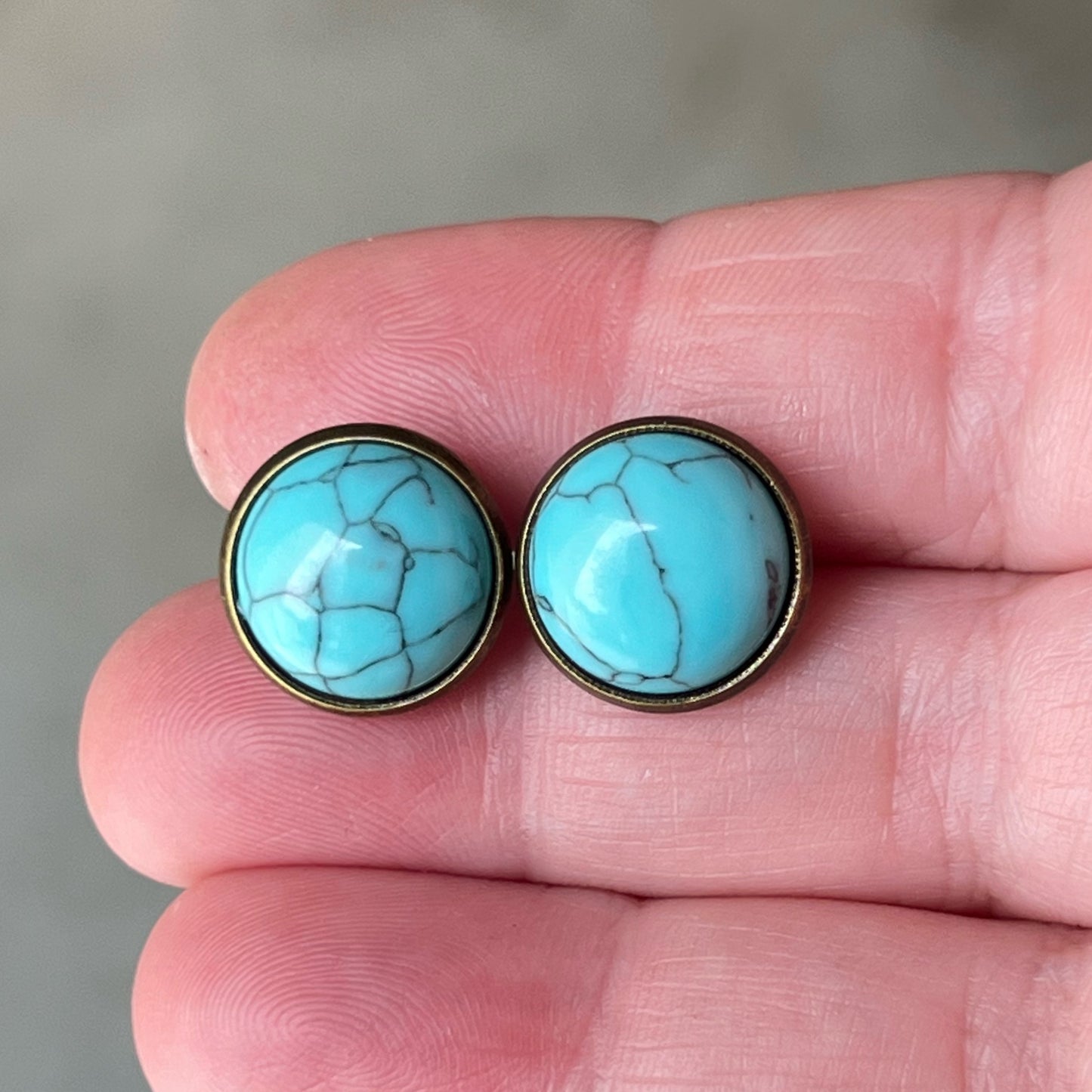 Round turquoise brass stud earrings in a hand for sizing reference 