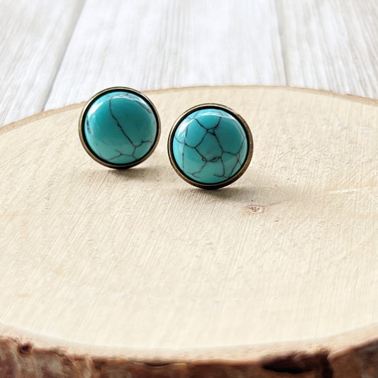 Round turquoise brass stud earrings displayed on a light wood background