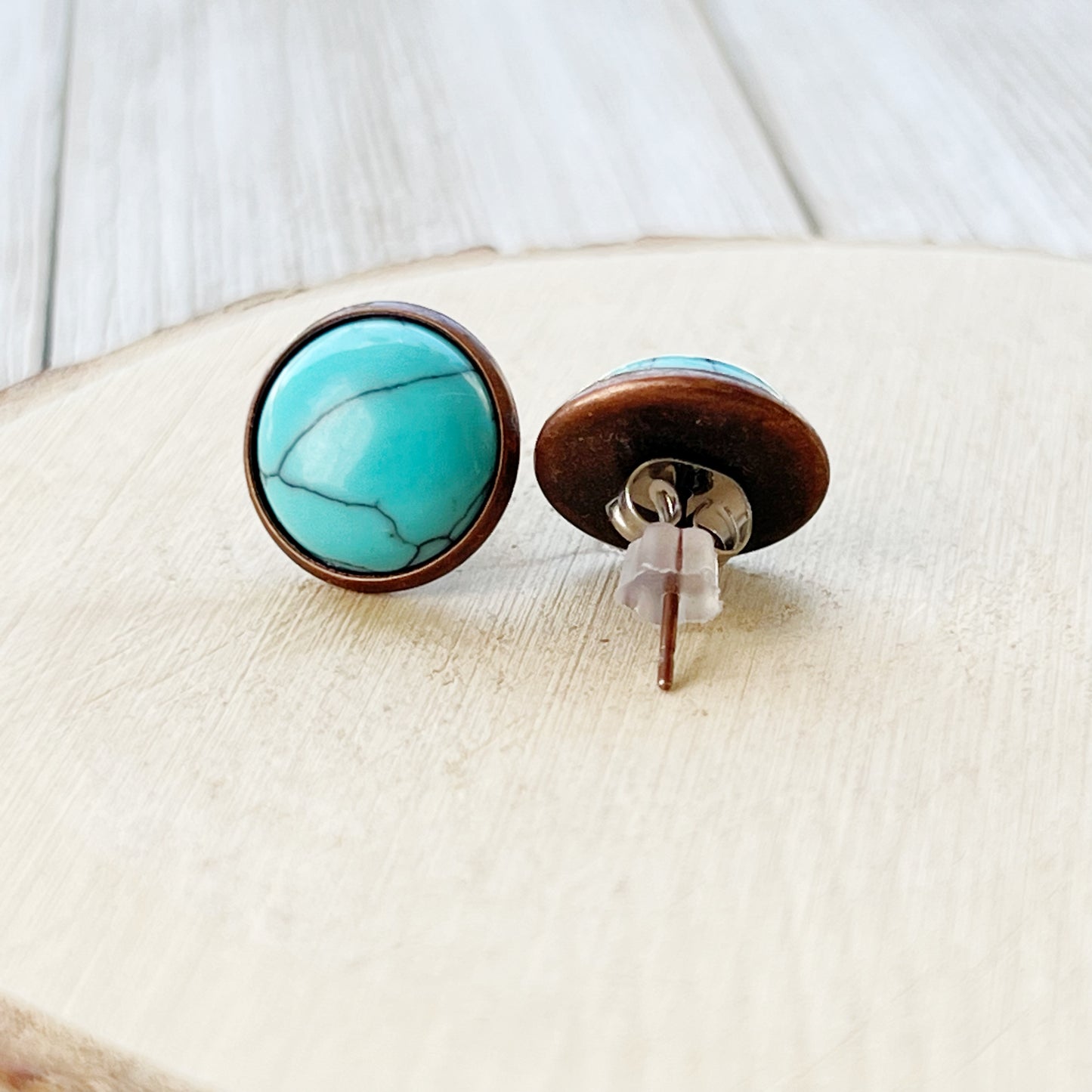 Back of round turquoise copper stud earrings displayed on a light wood background