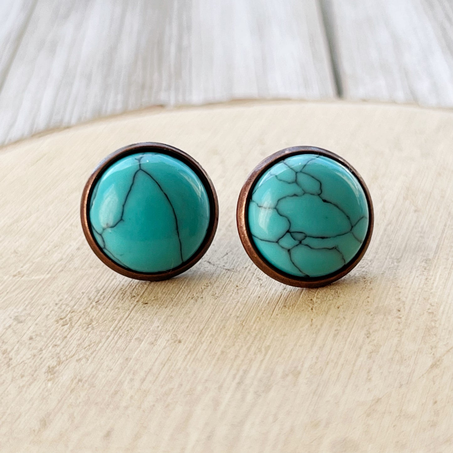 Close-up of round turquoise copper stud earrings displayed on a light wood background