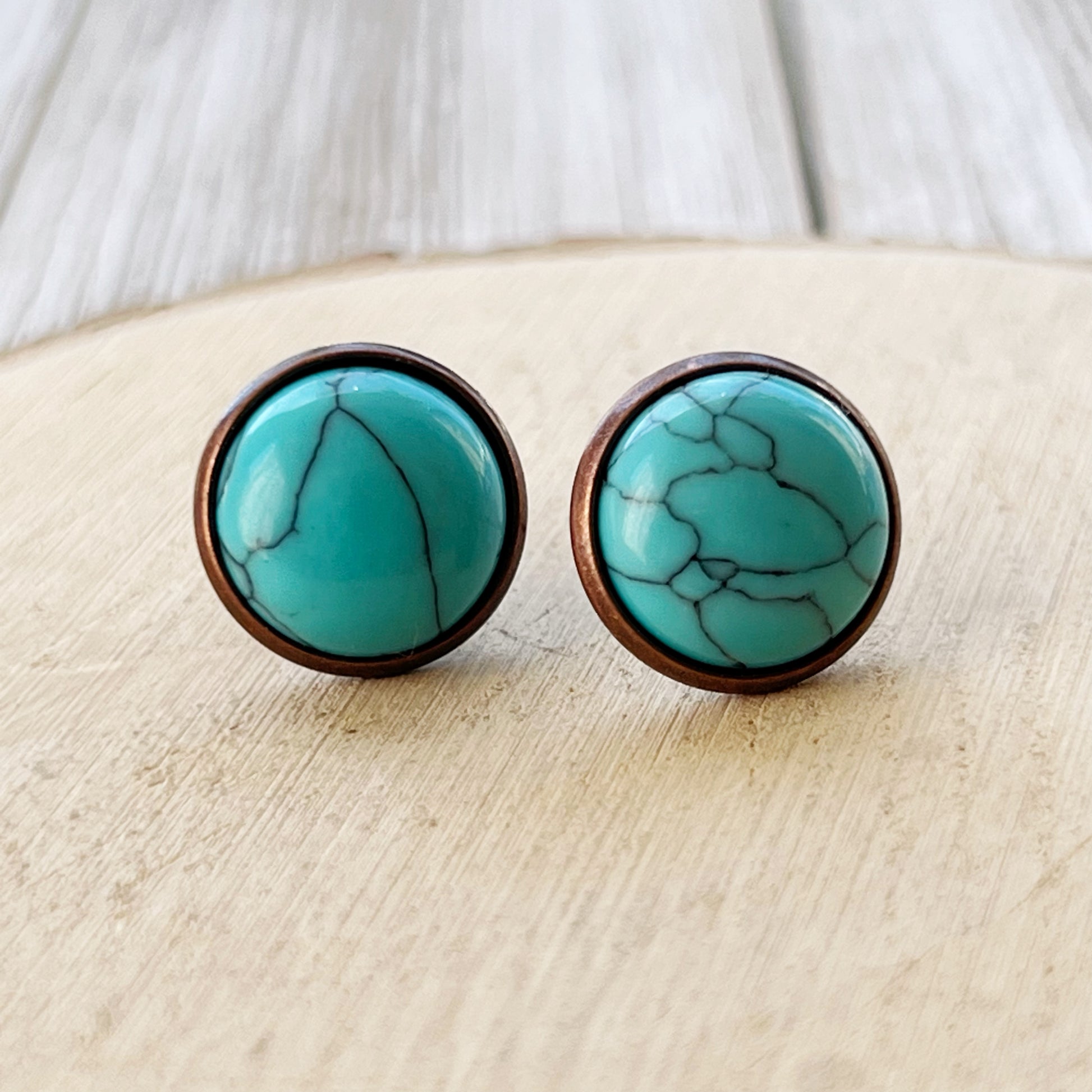 Close-up of round turquoise copper stud earrings displayed on a light wood background