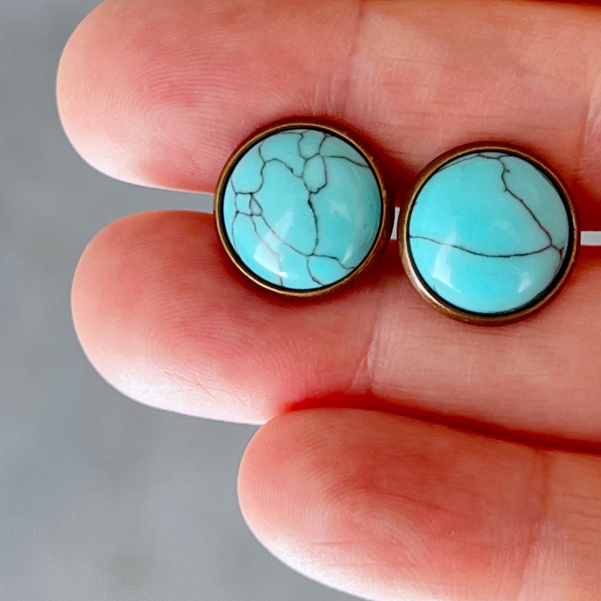 Round turquoise copper stud earrings in hand for sizing scale 