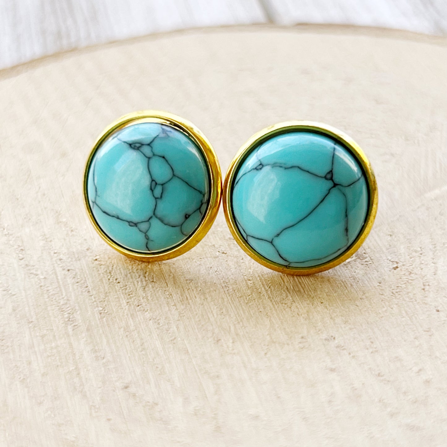 Round turquoise gold stud earrings displayed on a light wood slice background