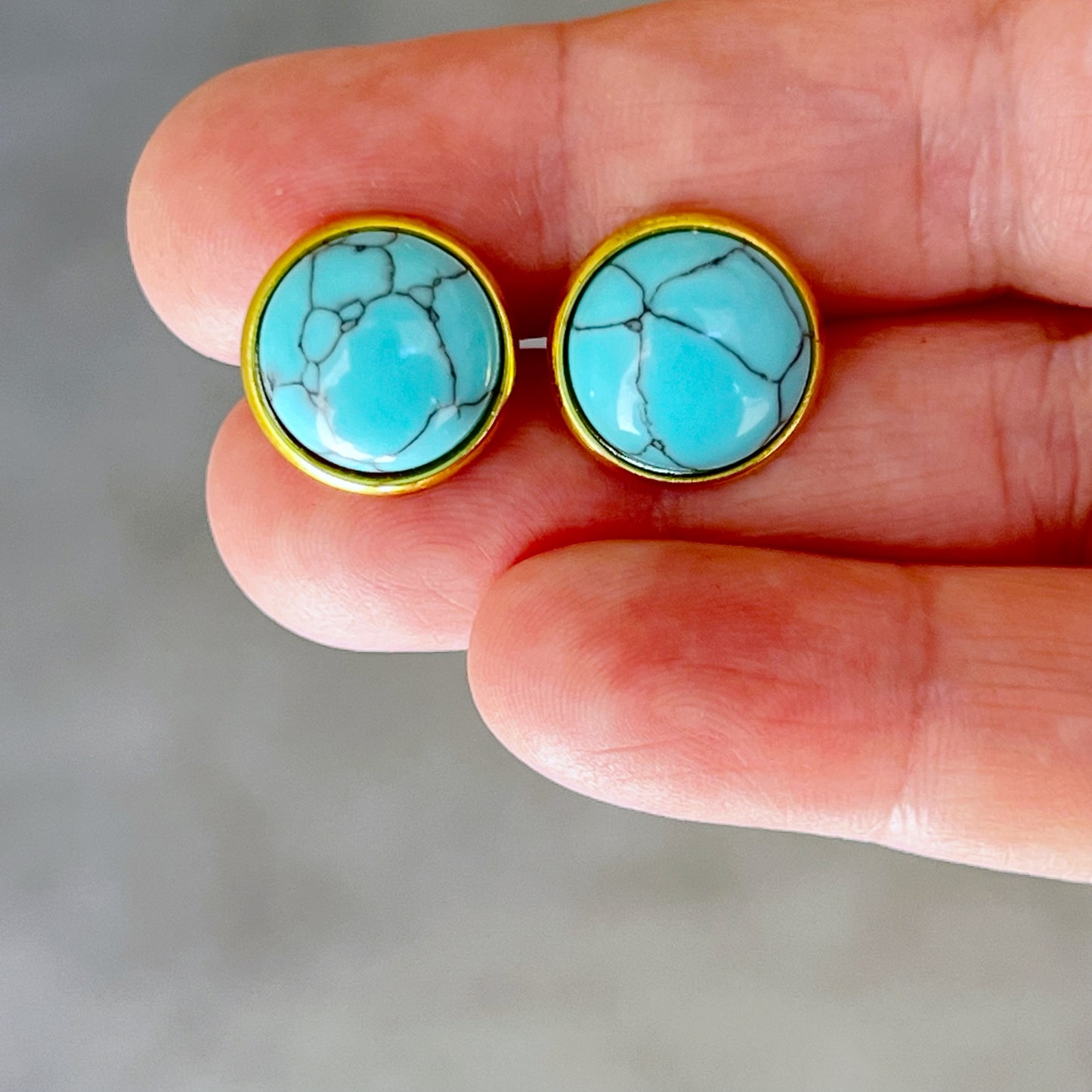 Round turquoise gold stud earrings displayed in hand for sizing scale 