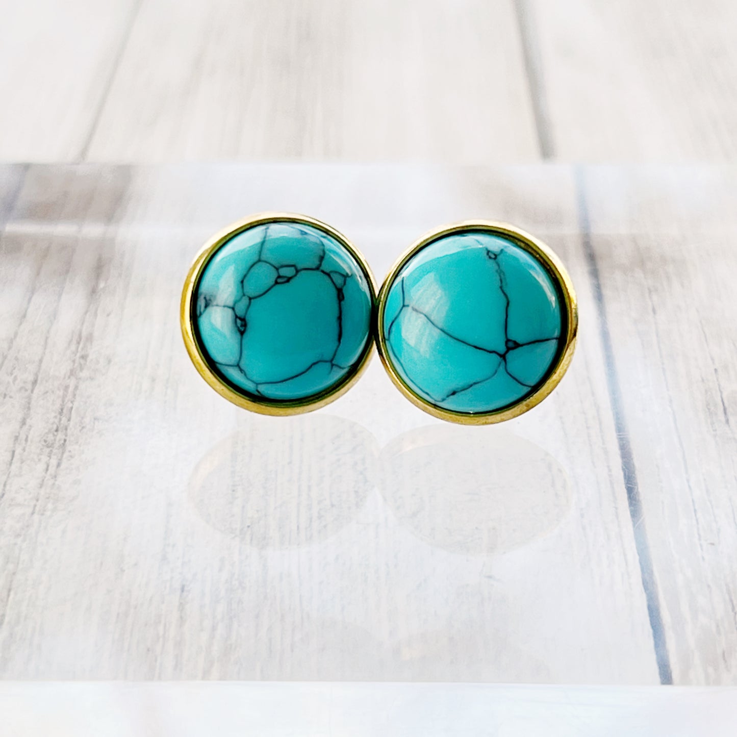 Round turquoise gold stud earrings on a clear riser