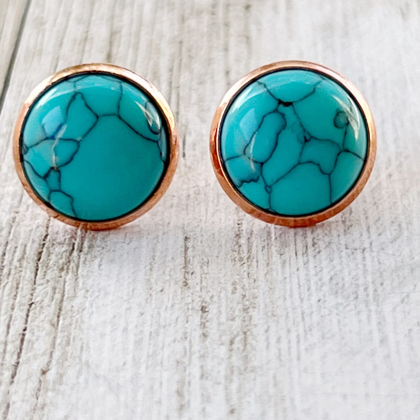 Round turquoise rose gold stud earrings displayed on a wooden surface - close-up view