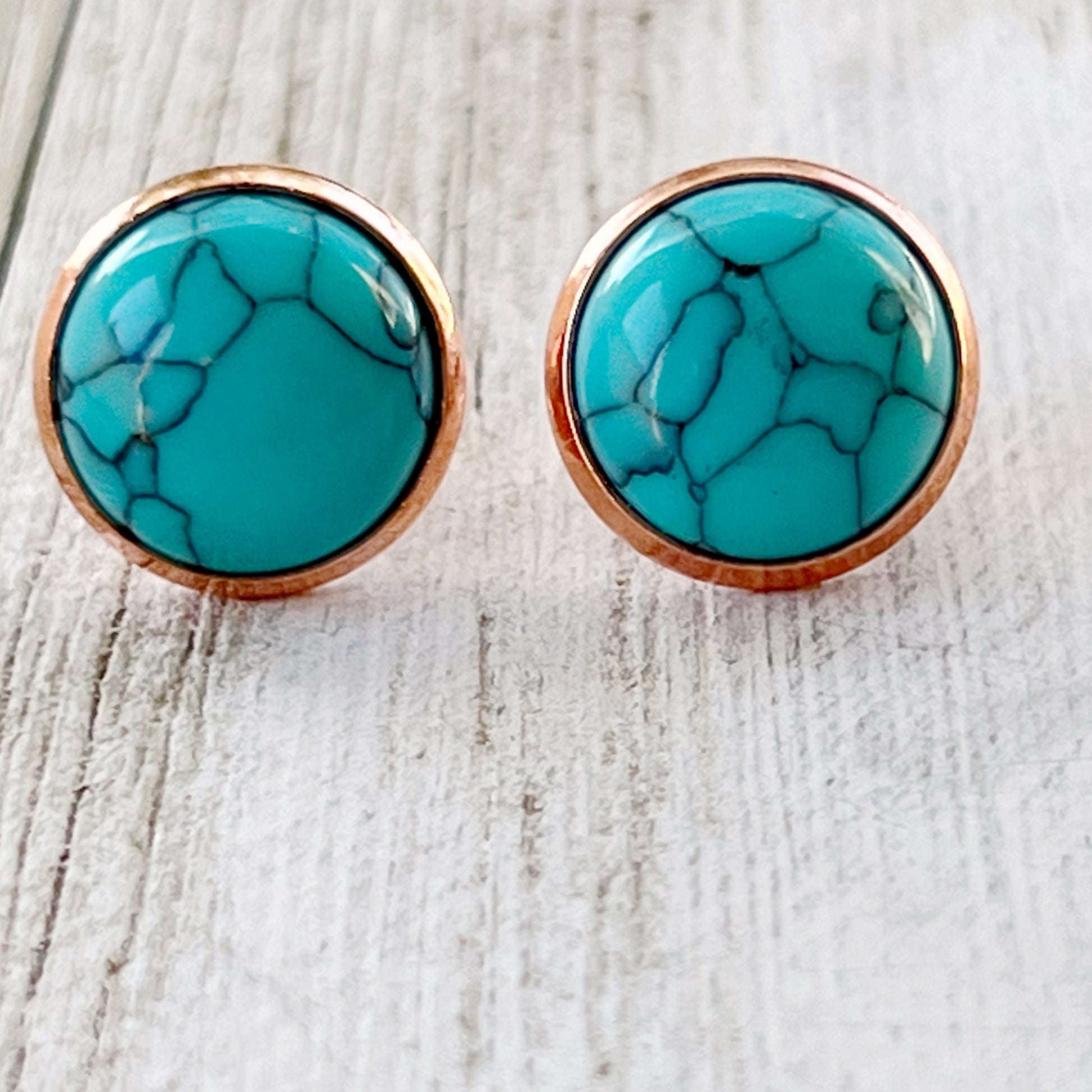 Round turquoise rose gold stud earrings displayed on a wooden surface - close-up view
