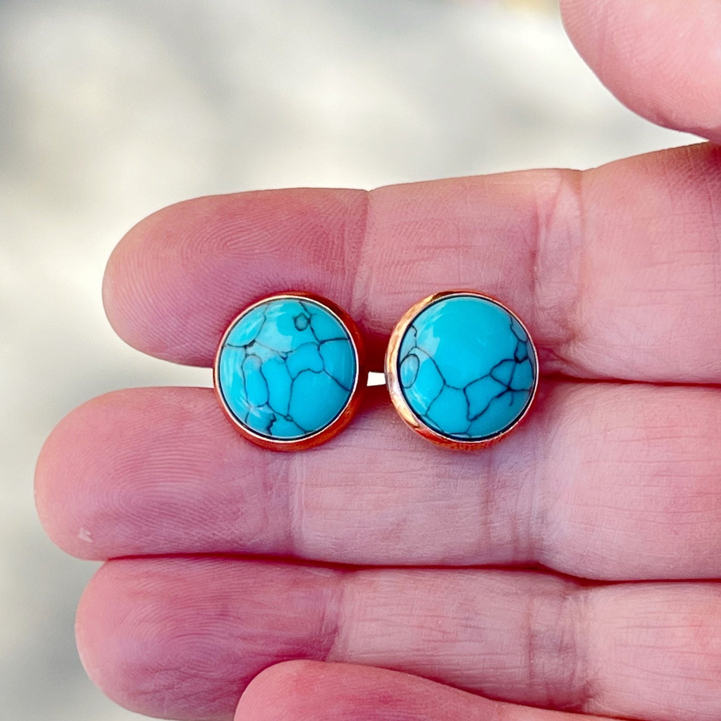 Round turquoise rose gold stud earrings displayed in a hand for scale 