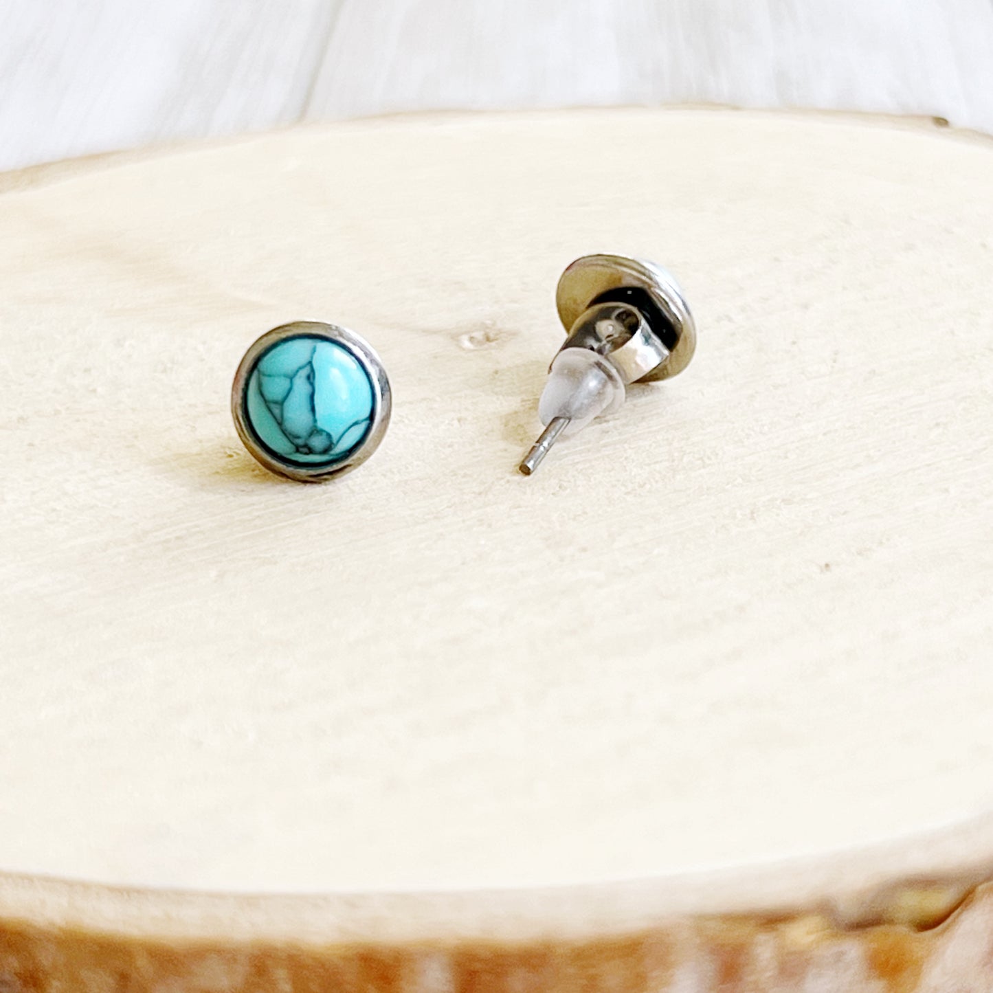 Small round turquoise stud earrings in a silver-tone setting shown close up backside 