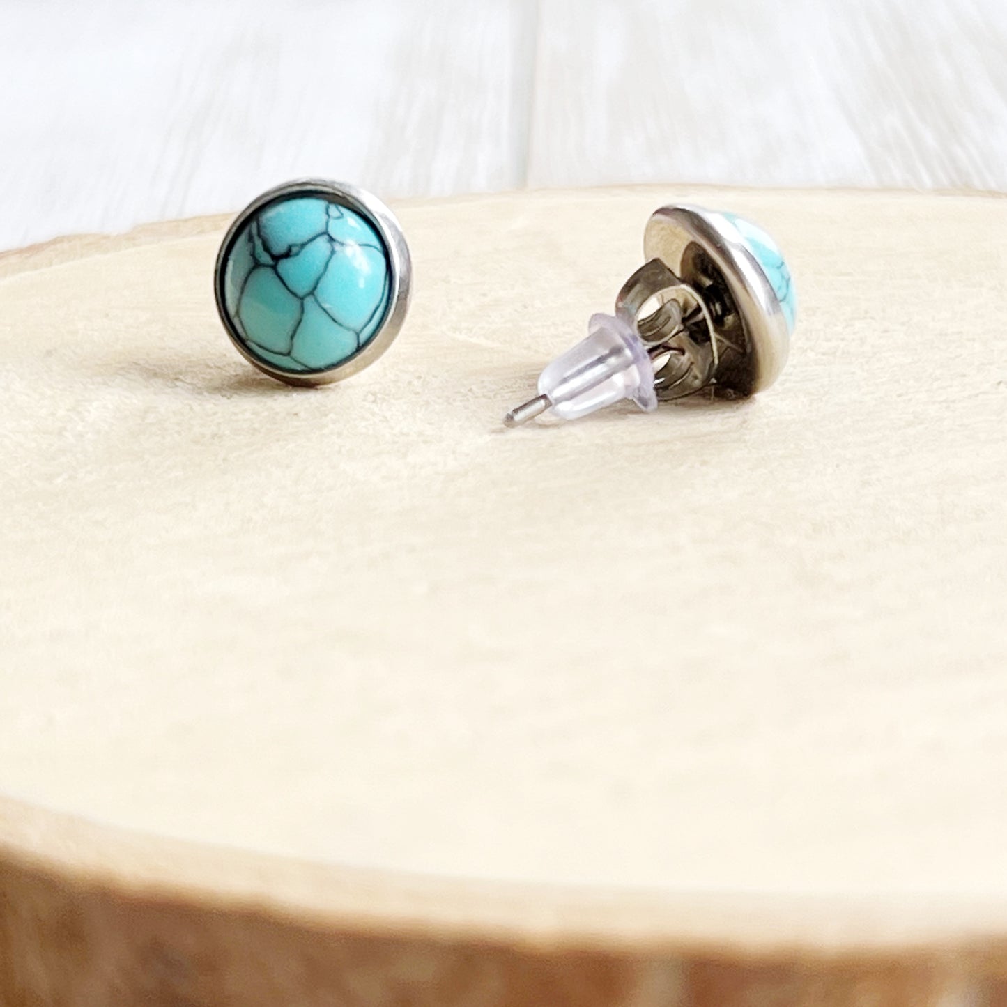 Back of Round turquoise stud earrings in a silver-tone setting displayed on a light wood background