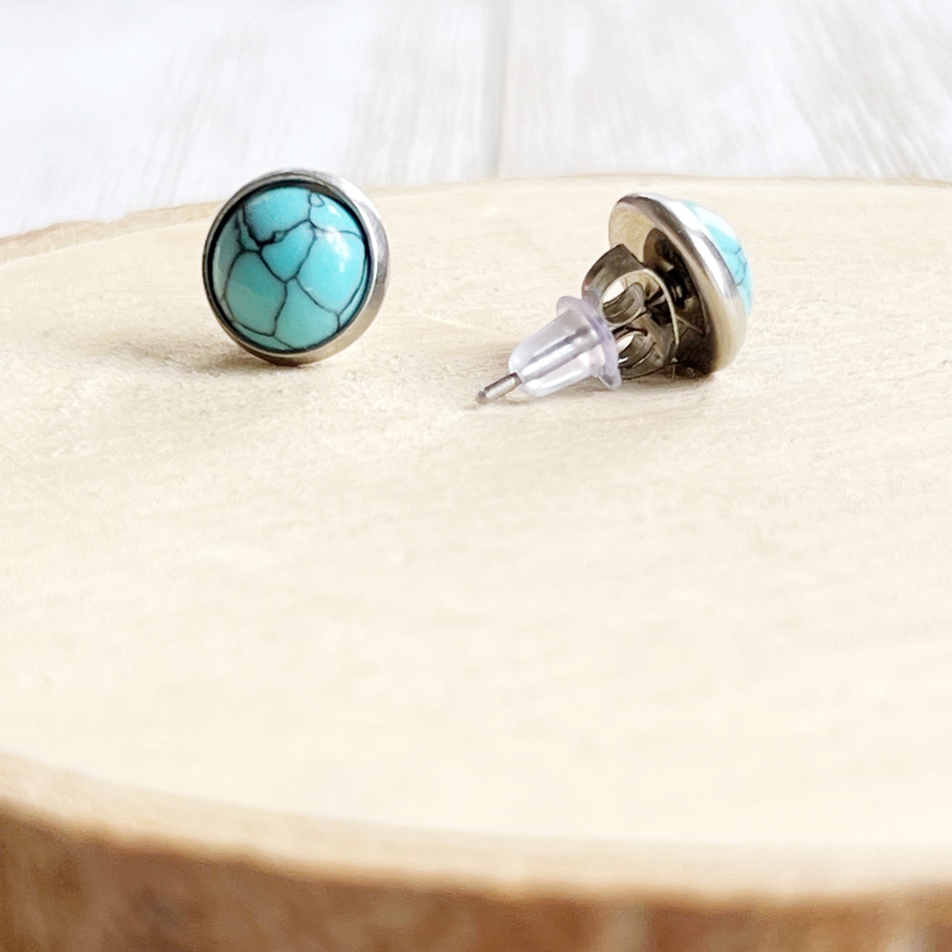 Back of Round turquoise stud earrings in a silver-tone setting displayed on a light wood background