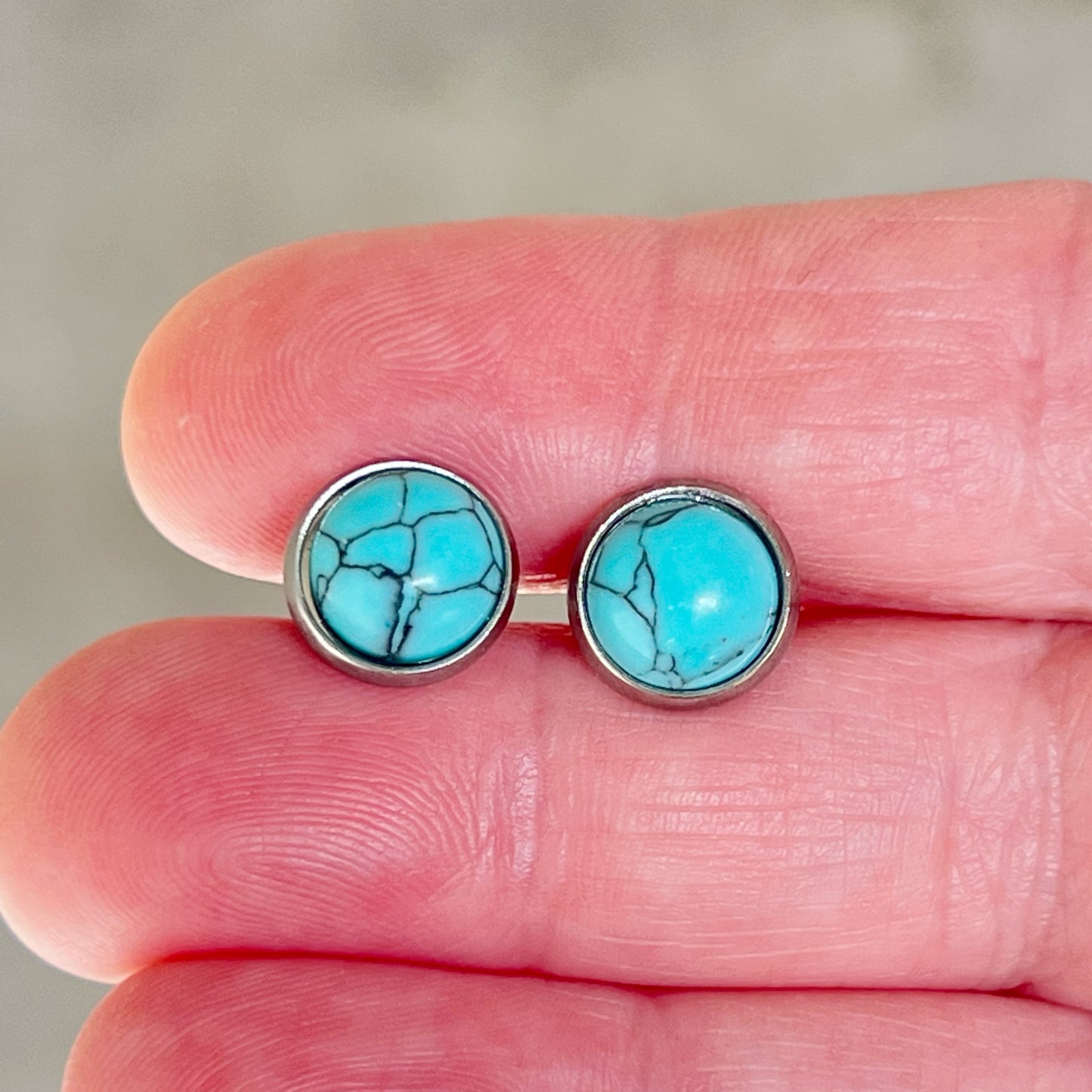 Round turquoise stud earrings in a silver-tone setting in hand for sizing scale 