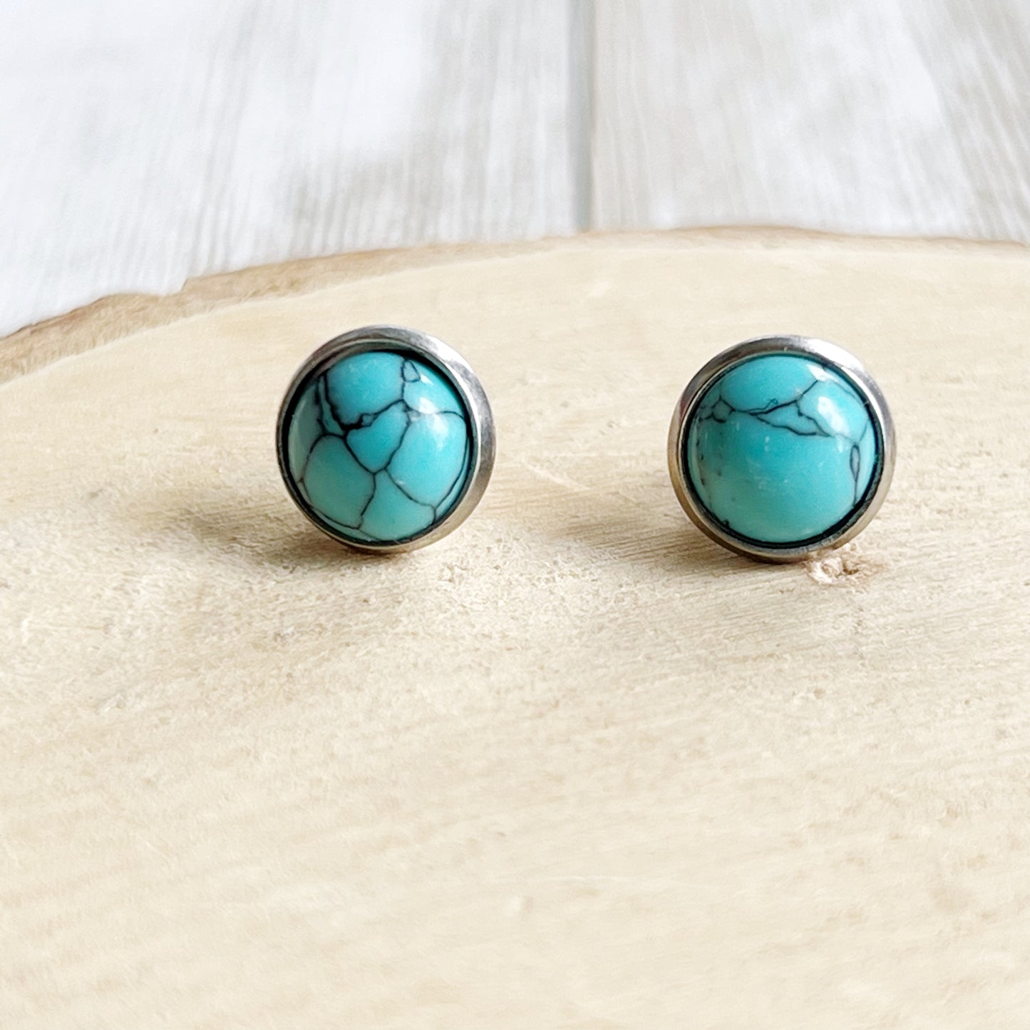 Round turquoise stud earrings in a silver-tone setting displayed on a light wood background