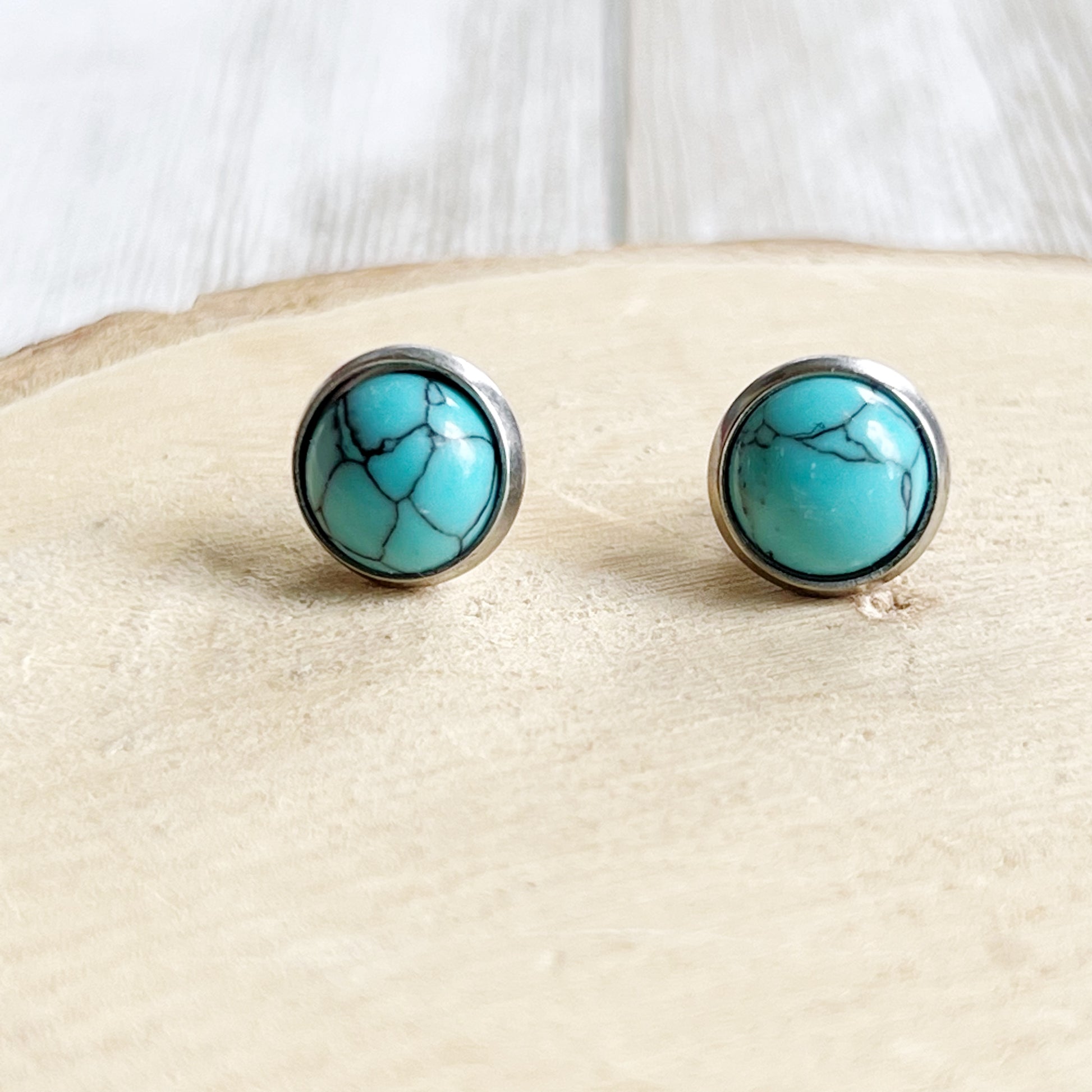 Round turquoise stud earrings in a silver-tone setting displayed on a light wood background