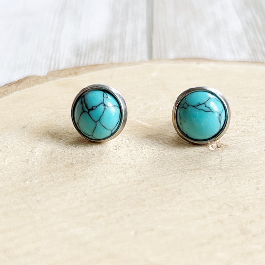 Round turquoise stud earrings in a silver-tone setting displayed on a light wood background