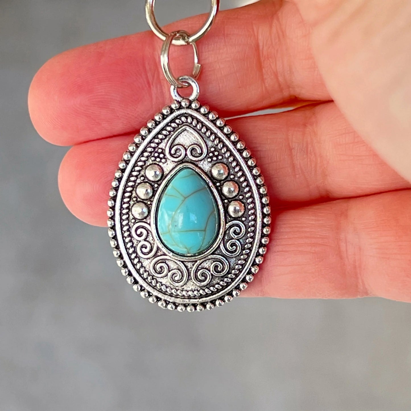 Silver western handbag charm with ornate medallion detail and faux turquoise accent in hand for scale 