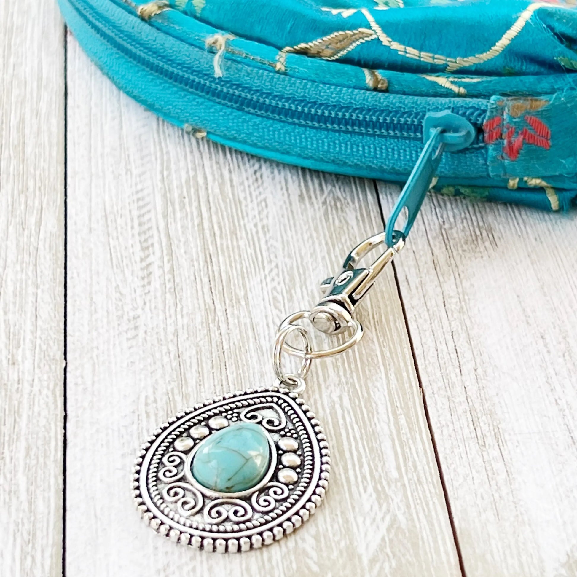 Silver western handbag charm with ornate medallion detail and faux turquoise accent on zipper of handbag 
