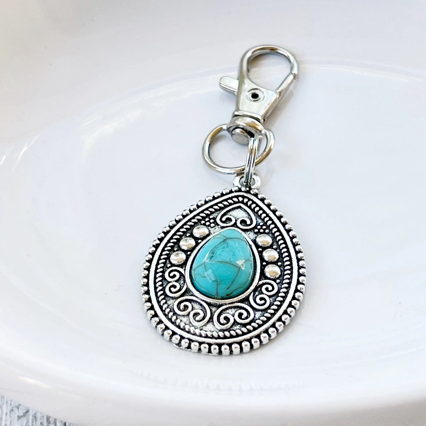 Silver western handbag charm with ornate medallion detail and faux turquoise accent on a white dish display