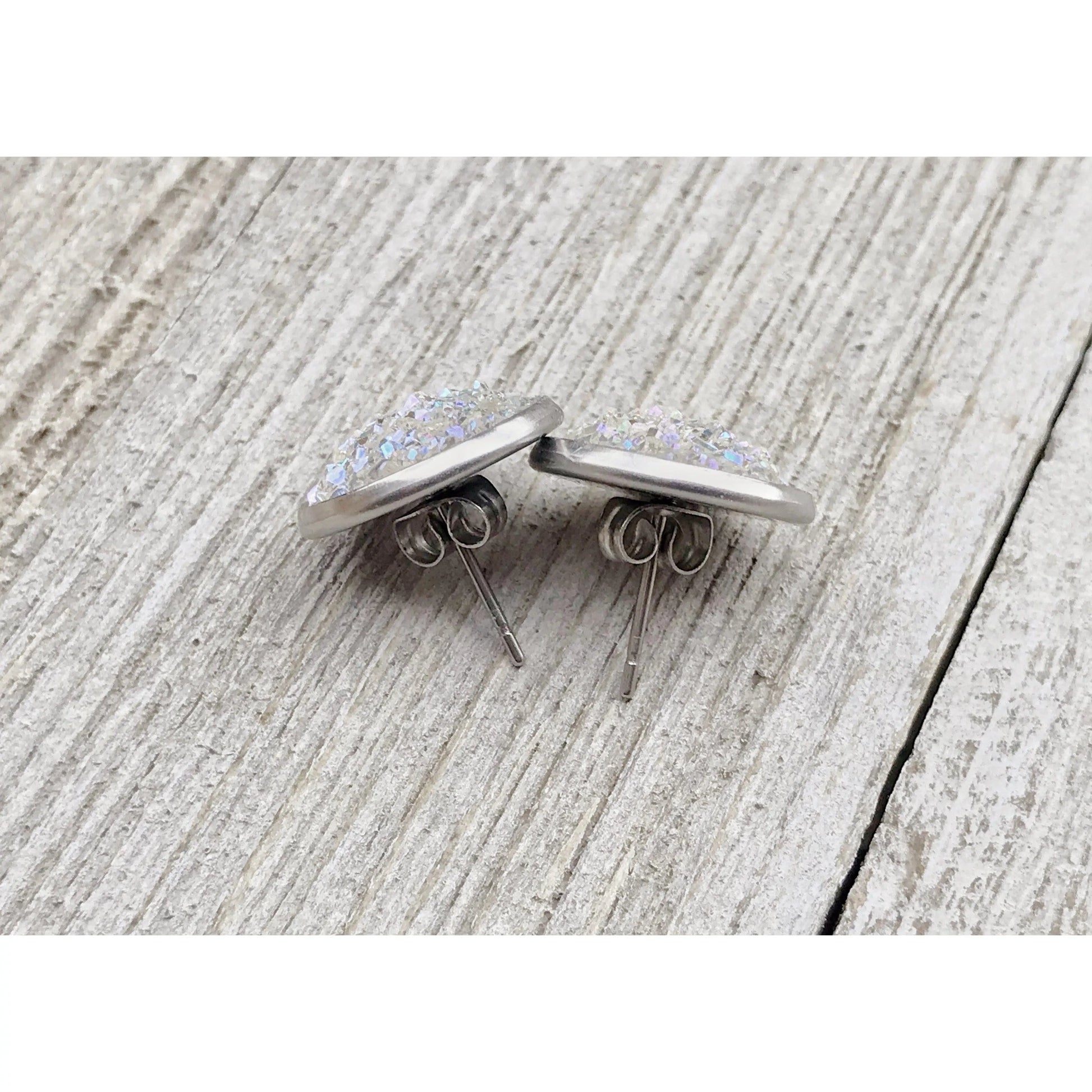 Back of a pair of silver earrings with glittery centers on a textured wooden surface