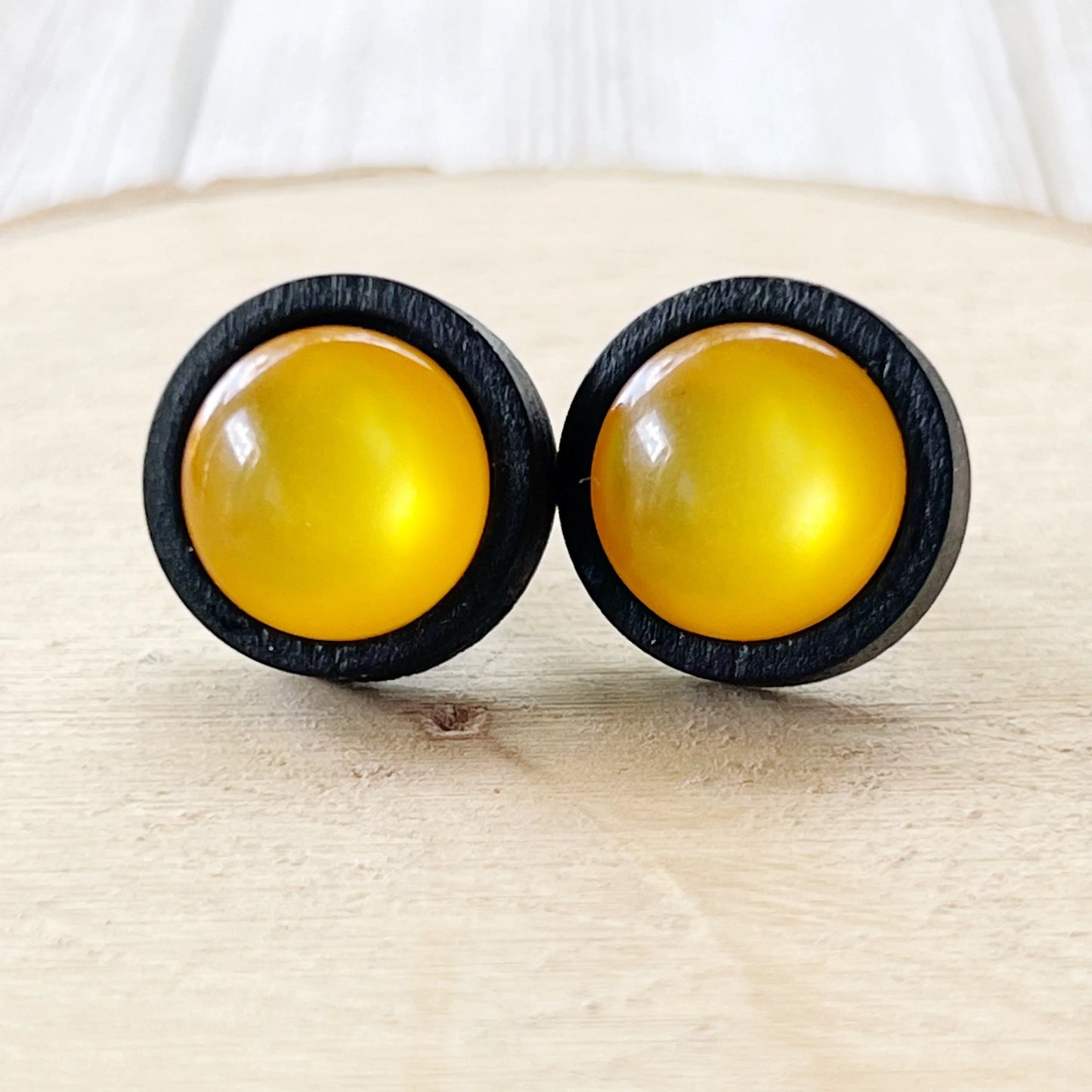 Pair of round earrings with yellow centers and black rims on a beige surface.