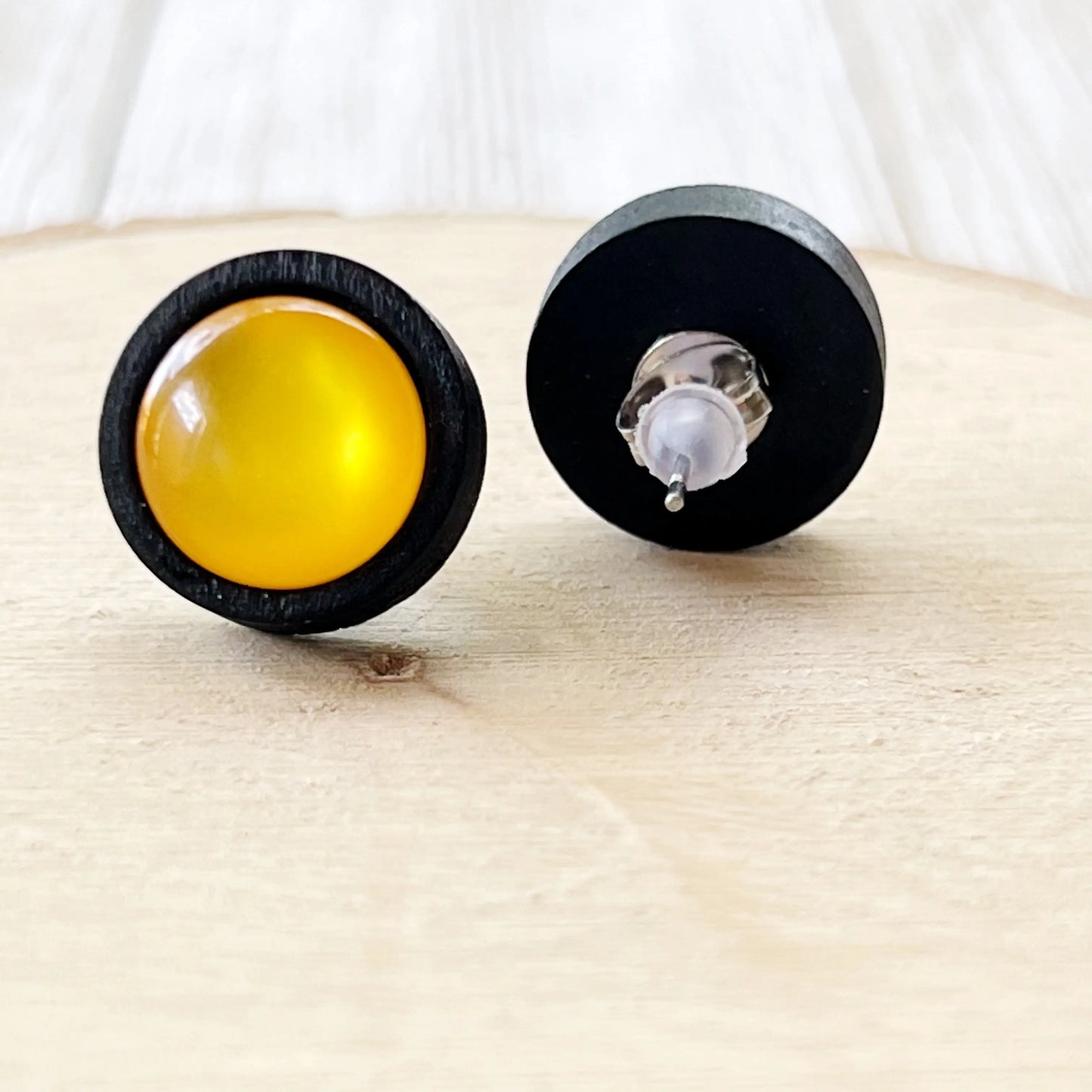 Pair of earrings with yellow and black designs on a light wooden surface showing the back of the earring.