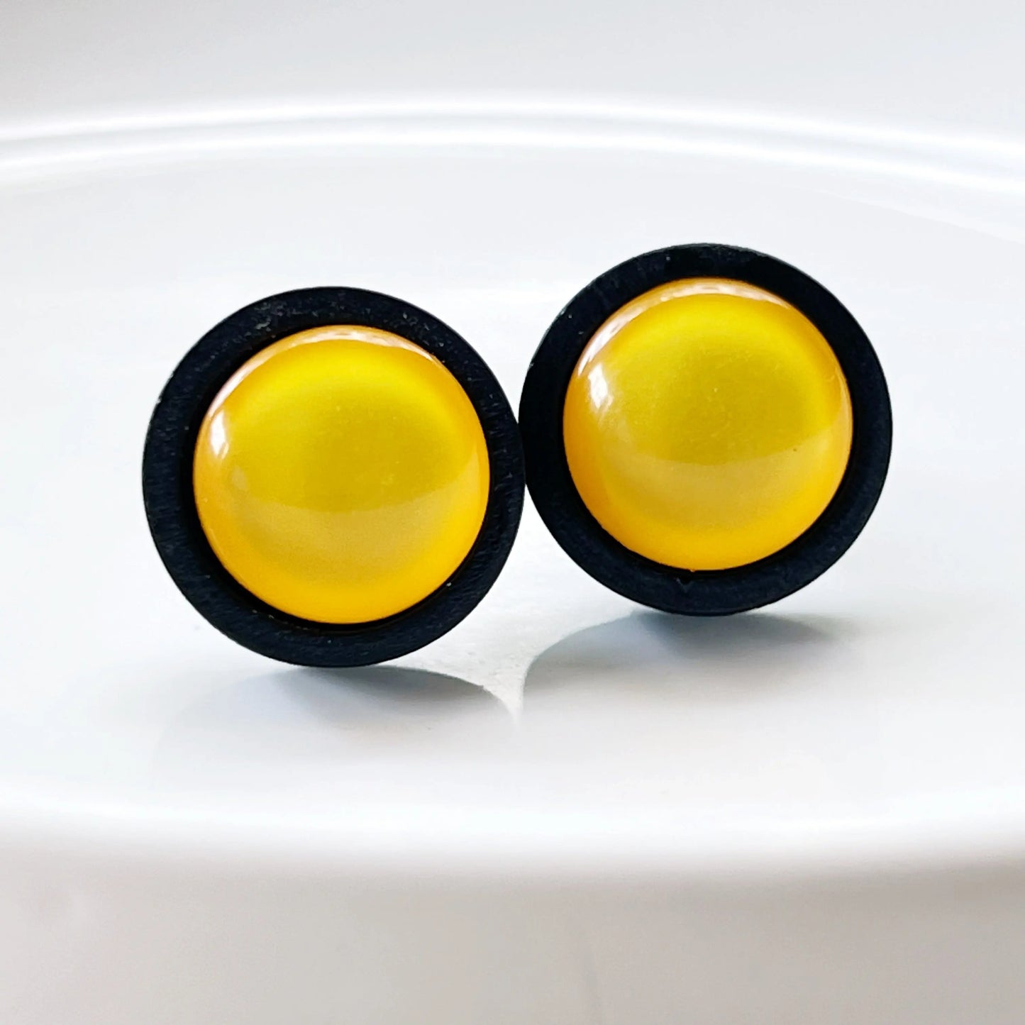 Pair of yellow round earrings with black rims on a white glass background