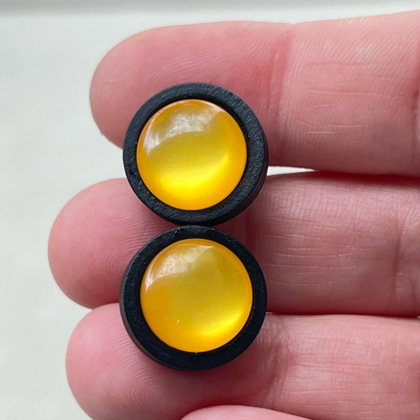 Two yellow round earrings with black borders held between fingers on a white background