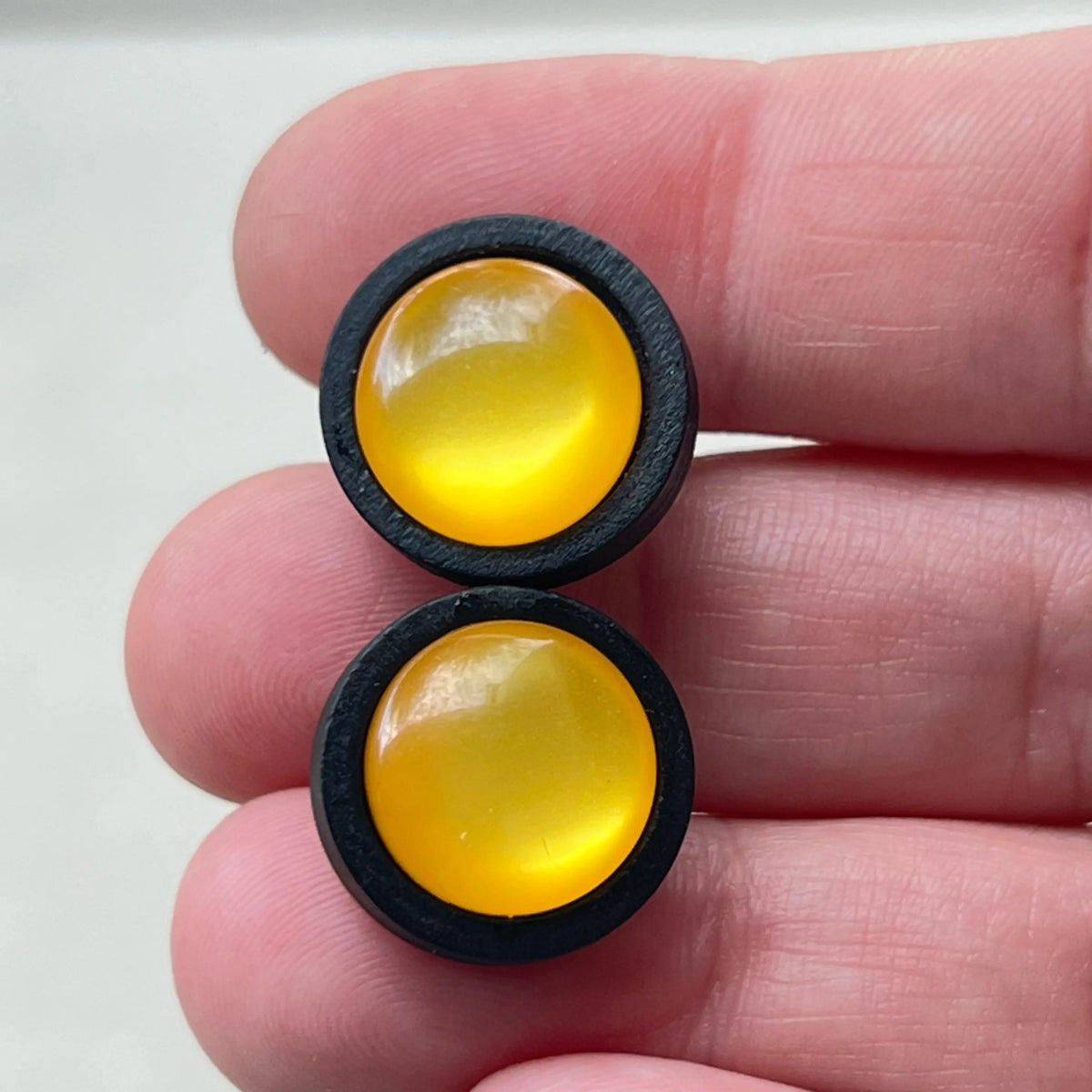 Two yellow round earrings with black borders held between fingers on a white background