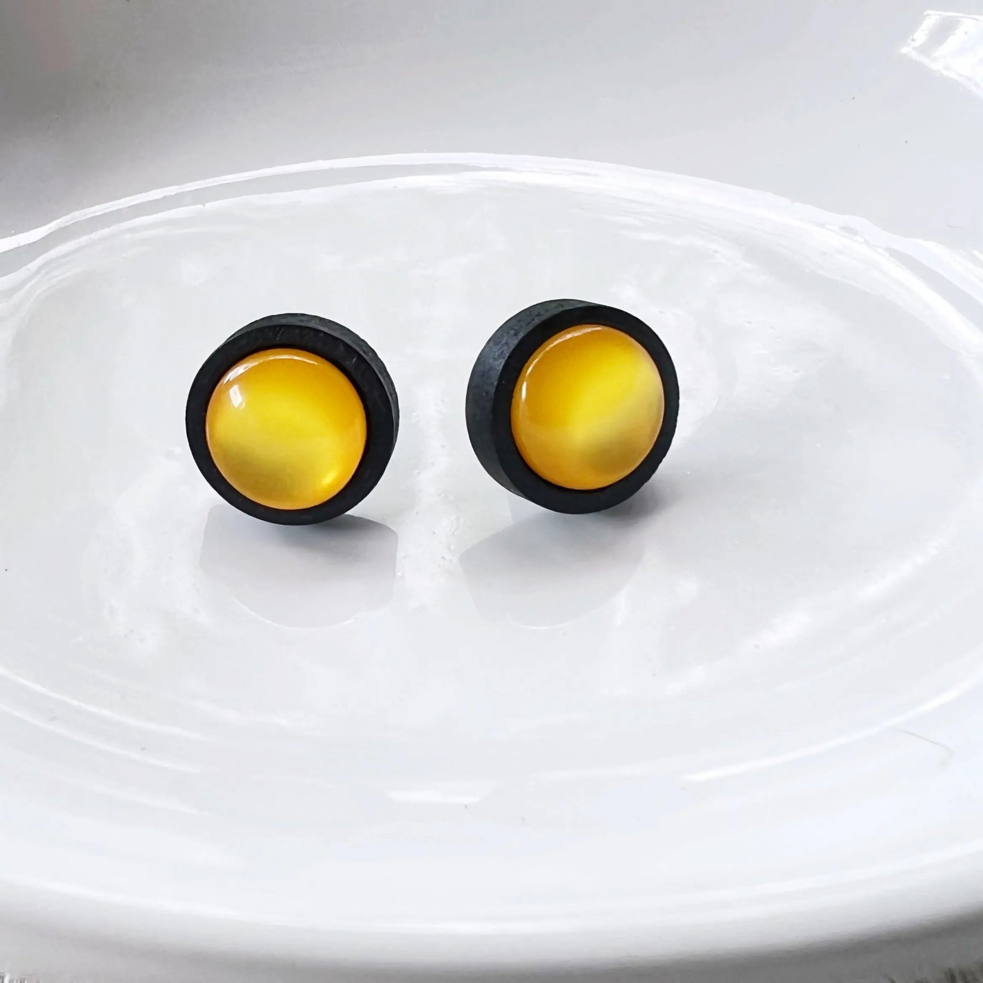 Pair of round earrings with yellow centers and black rims on a shiny white background